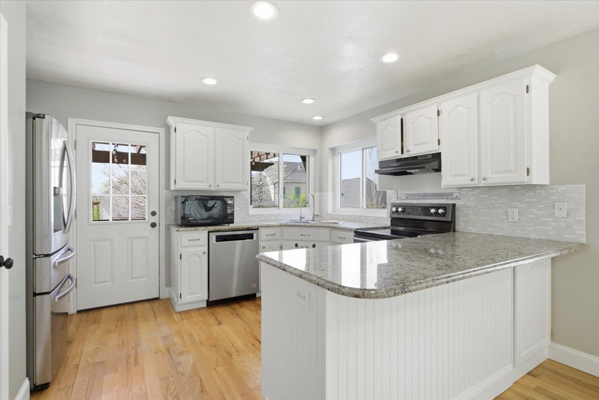 Kitchen with a peninsula, stainless steel appliances, decorative backsplash, white cabinetry, and light wood-style floors