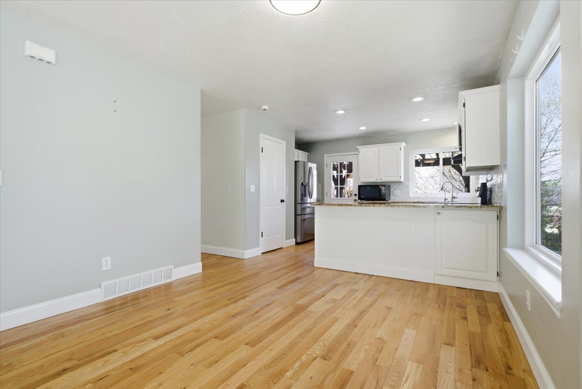 Kitchen with a peninsula, light wood finished floors, light stone countertops, white cabinets, and stainless steel fridge