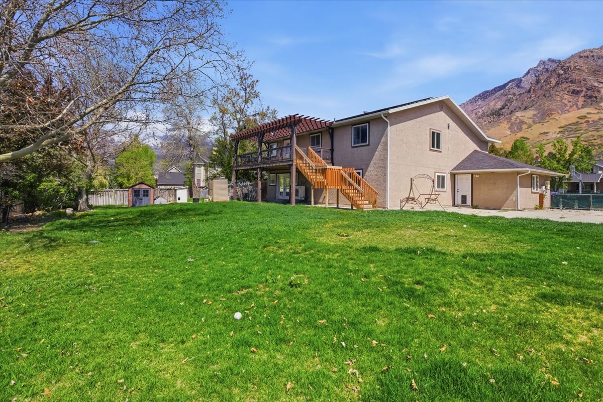 Back of house with stucco siding, a storage shed, a deck with mountain view, a patio, and a chimney