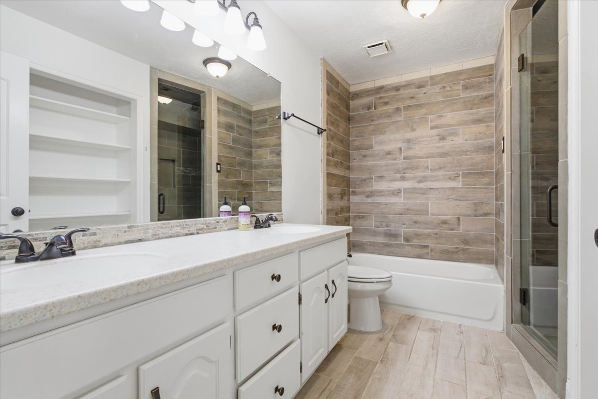 Full bathroom featuring double vanity, a stall shower, built in features, light wood-style floors, and a bath