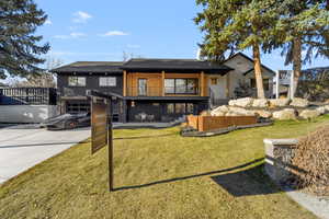 Back of property featuring a patio, concrete driveway, a yard, and a balcony