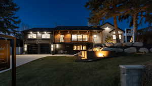 Back of house at twilight with concrete driveway, a garage, a lawn, and a balcony