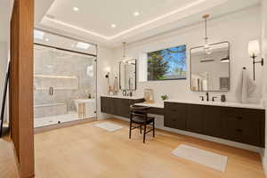 Full bath featuring two vanities, a marble finish shower, light wood-style floors, a tray ceiling, and recessed lighting