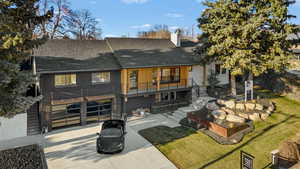 Rear view of house with a shingled roof, driveway, a balcony, and a chimney