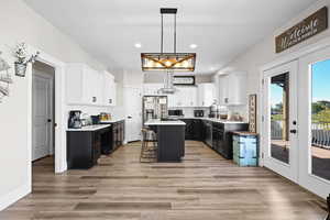 Dual tone kitchen with two tone cabinetry, a kitchen island, a kitchen breakfast bar, decorative backsplash, and hanging light fixtures