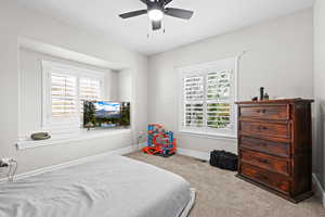 Carpeted bedroom with ceiling fan and multiple windows