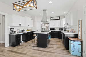 Kitchen with two tone cabinetry, a kitchen breakfast bar, a kitchen island, stainless steel appliances, and island range hood