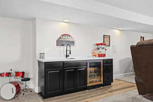 Indoor wet bar featuring dark cabinetry, beverage cooler, and light wood-type flooring