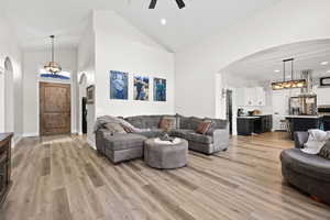 Living room featuring arched walkways, hanging lights, a ceiling fan, light wood finished floors, and vaulted ceiling