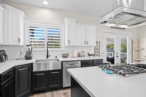Kitchen featuring french doors, ventilation hood, stainless steel appliances, light stone countertops, and two tone color scheme