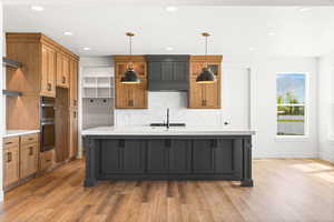 Two tone kitchen with two tone cabinetry, an island with sink, light wood-style floors, double oven, and tasteful backsplash