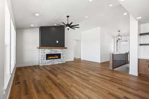 Unfurnished living room featuring a fireplace, dark wood finished floors, lofted ceiling, a ceiling fan, and suspended lighting