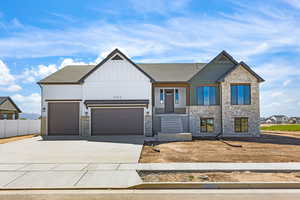 View of front of house with stone siding, board and batten siding, an attached garage, driveway, and roof with shingles