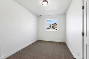 Empty room featuring baseboards and dark carpet