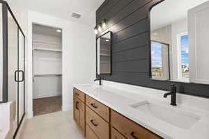 Bathroom with double vanity, a stall shower, a spacious closet, and light tile patterned floors