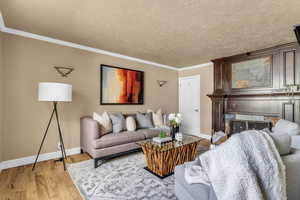 Living room with light wood-type flooring, ornamental molding, a tiled fireplace, and a textured ceiling