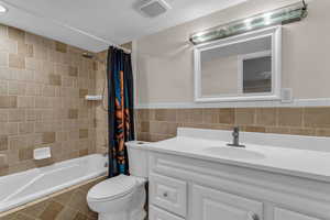 Full bathroom with vanity, shower / bath combo, and tile walls