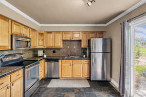 Kitchen with stainless steel appliances, dark stone finish flooring, tasteful backsplash, light wood finish cabinetry, and crown molding