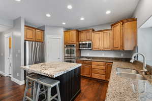 Kitchen with light stone countertops, a kitchen breakfast bar, stainless steel appliances, a center island, and wood finish cabinetry
