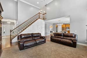 Living area featuring a chandelier, ornamental molding, a high ceiling, washer / dryer, and light colored carpet