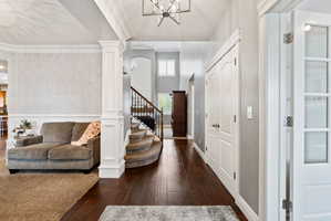 Foyer entrance featuring dark wood-type flooring, a chandelier, ornamental molding, and decorative columns