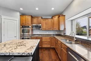 Kitchen with stainless steel appliances, light stone countertops, wood finish cabinetry, recessed lighting, and dark wood-style flooring