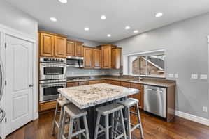 Kitchen with stainless steel appliances, wood finish cabinets, a kitchen breakfast bar, a center island, and dark wood-type flooring
