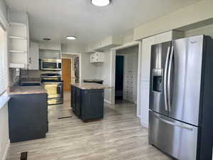 Two tone kitchen with dual tone cabinets, stainless steel appliances, light wood-style flooring, open shelves, and decorative backsplash