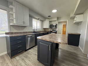 Two tone kitchen featuring dark countertops, two tone cabinetry, stainless steel appliances, light wood finished floors, and a kitchen breakfast bar