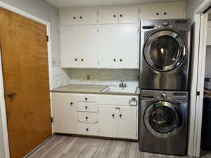Laundry area featuring stacked washer / dryer, cabinet space, and light wood-style floors