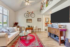 Living room with light wood-style flooring, lofted ceiling, and a ceiling fan