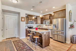 Kitchen featuring stainless steel appliances, a breakfast bar area, light wood finished floors, pendant lighting, and a kitchen island