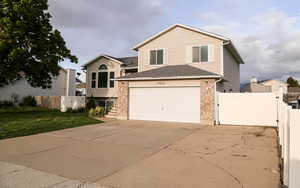 View of front facade with a gate, driveway, brick siding, and roof with shingles