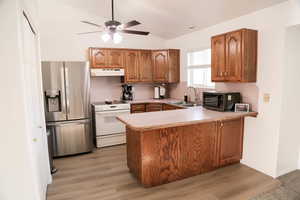 Kitchen with wood finish cabinetry, stainless steel fridge with ice dispenser, light countertops, white range with electric cooktop, and black microwave
