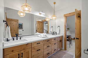 Bathroom with double vanity, vaulted ceiling, hanging lights, and light colored carpet