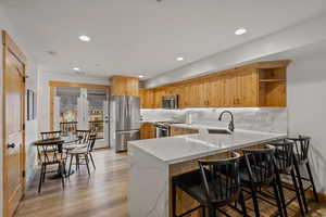 Kitchen featuring a peninsula, light stone counters, stainless steel appliances, a breakfast bar area, and light wood finished floors