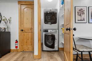 Laundry area with light wood finished floors and stacked washer / dryer