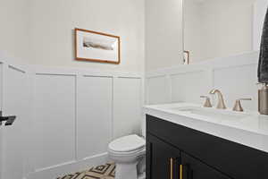 Half bathroom with vanity, a decorative wall, and a wainscoted wall