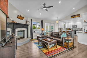 Living area featuring recessed lighting, a ceiling fan, a glass covered fireplace, light wood-type flooring, and vaulted ceiling