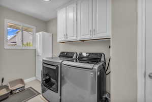 Laundry room with washer and dryer, cabinet space, and light tile patterned flooring