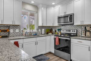 Kitchen featuring stainless steel appliances, white cabinets, light stone counters, light wood-style flooring, and tasteful backsplash
