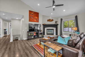 Living area with wood finished floors, vaulted ceiling, ceiling fan, a glass covered fireplace, and recessed lighting