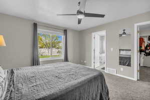 Bedroom featuring light colored carpet, ceiling fan, ensuite bathroom, and a walk in closet