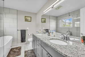 Full bathroom with a soaking tub, tile walls, double vanity, light tile patterned floors, and a shower with shower door