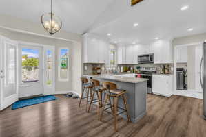 Kitchen featuring a kitchen bar, light stone countertops, stainless steel appliances, white cabinetry, and a peninsula