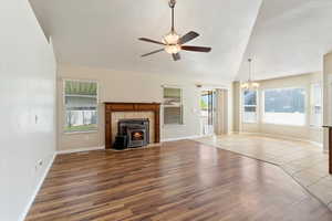Living room with a ceiling fan, hanging lights, wood finished floors, a tile fireplace, and vaulted ceiling
