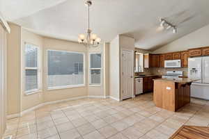 Kitchen featuring light tile patterned floors, dark stone countertops, white appliances, hanging lights, and a center island