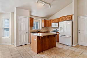 Kitchen featuring white appliances, light stone countertops, backsplash, wood finish cabinets, and a kitchen breakfast bar
