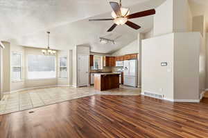 Kitchen with open floor plan, a center island, wood finish cabinets, white appliances, and light wood-style floors