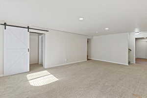Basement with a barn door, light carpet, and recessed lighting
